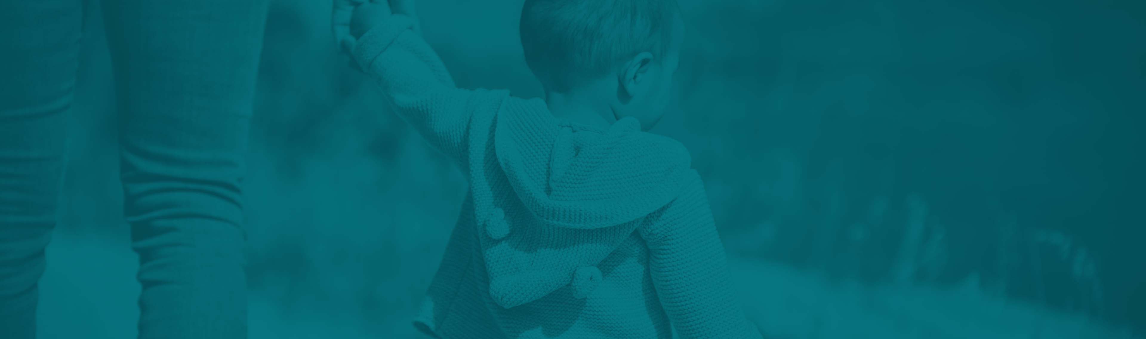 A baby walking with it's parent or gardian while holding hands.